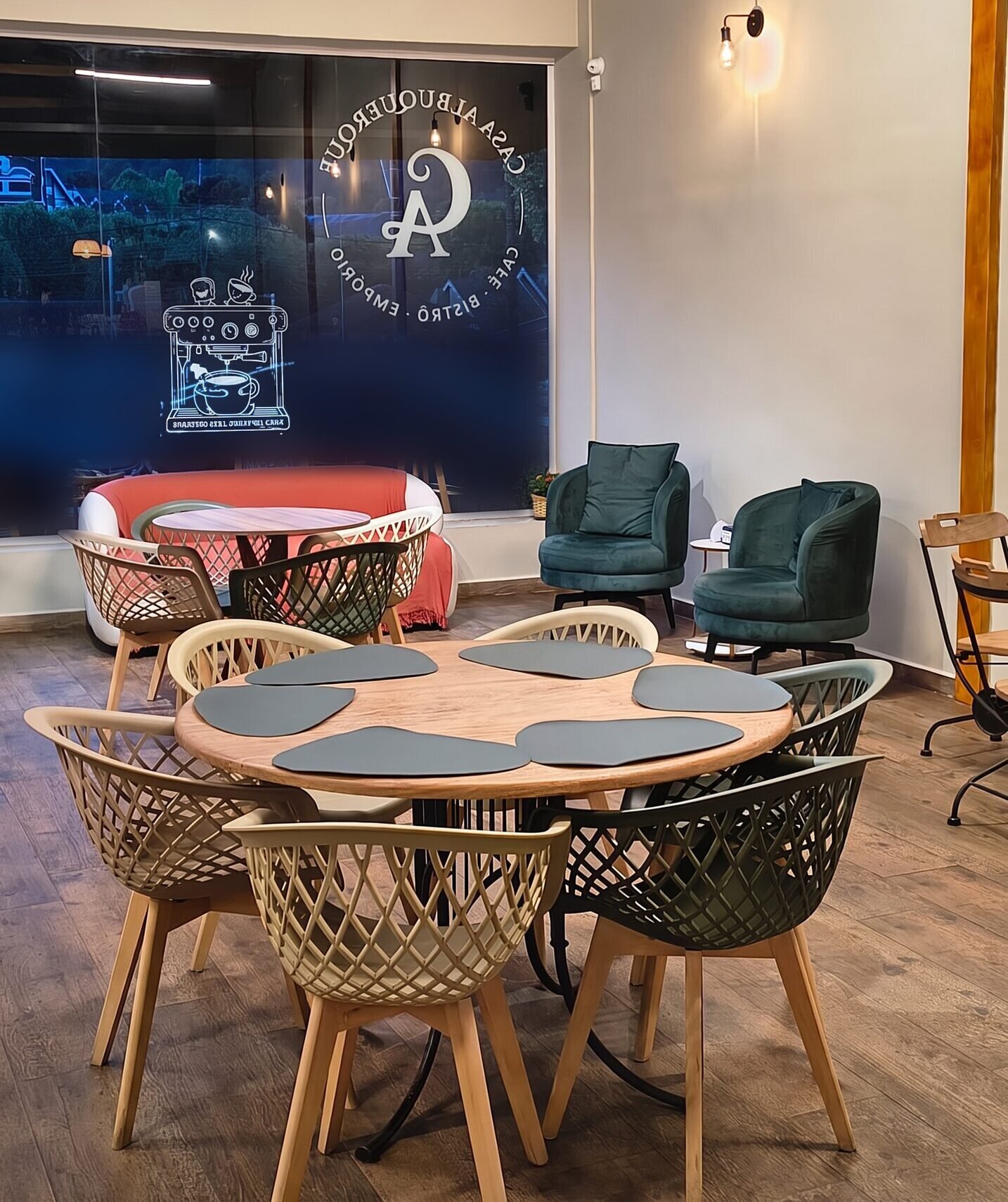 Salão da Casa Albuquerque em Campos do Jordão, com poltronas verdes, sofá coral e o logo da casa no vidro